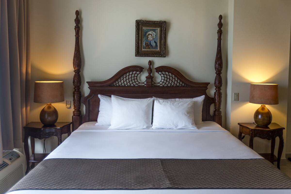 A large bed with a wooden headboard, two bedside tables with lamps, and a framed picture on the wall.