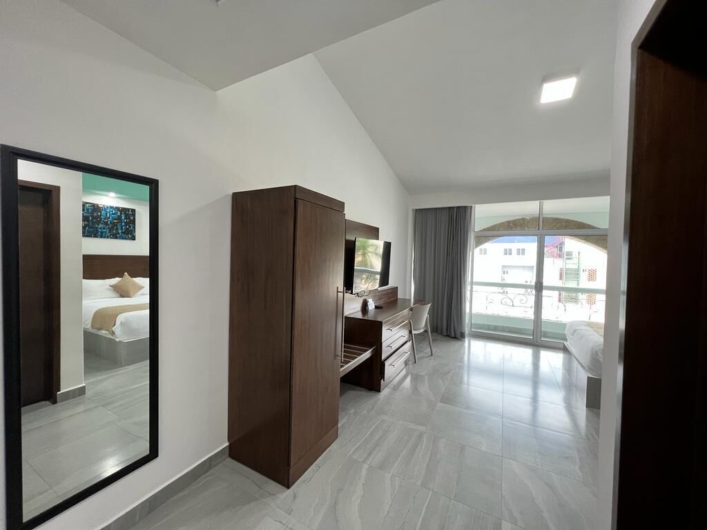 A modern hotel room with a large mirror, a wardrobe, a desk with a chair, and a balcony with a view.