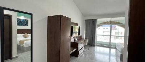 A modern hotel room with a large mirror, a wardrobe, a desk with a chair, and a balcony with a view.