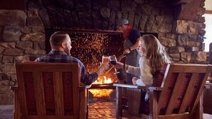 A cozy indoor setting with a stone fireplace, wooden furniture, and a person tending to the fire. - Glacier Park Lodge (East Glacier Park)