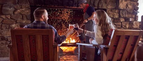 A cozy indoor setting with a stone fireplace, wooden furniture, and a person tending to the fire.