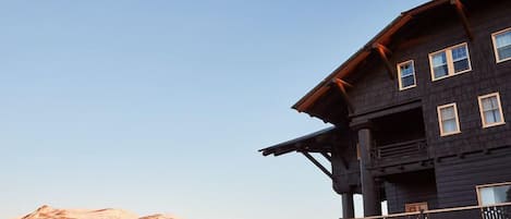 Edificio de madera de dos pisos con balcón, con montañas al fondo.
