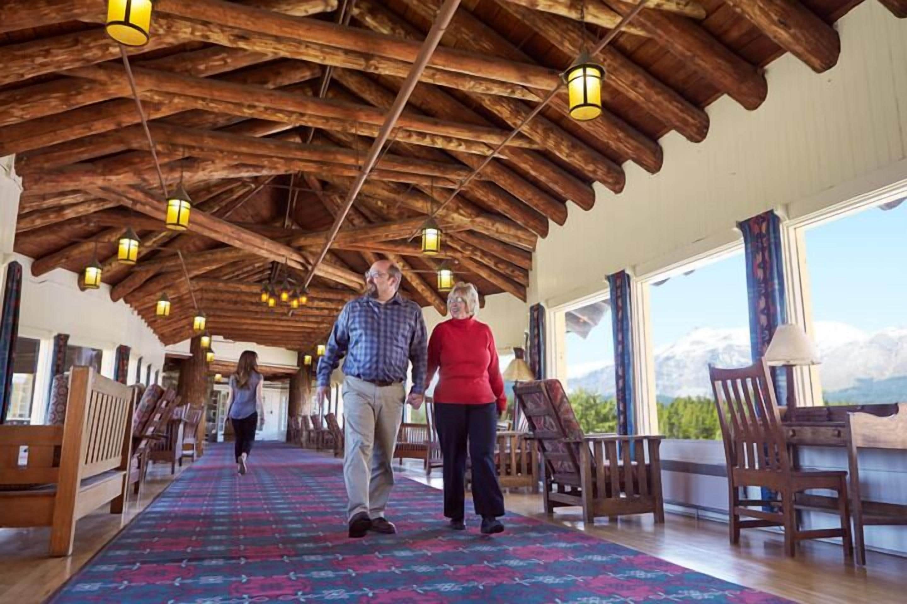 A spacious hall with wooden beams and benches, large windows with a mountain view, and hanging lanterns.