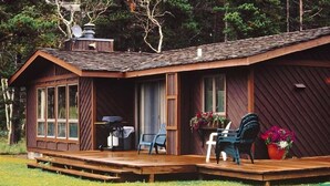 A rustic cabin with a wooden deck, large windows, and outdoor seating. - Glacier Park Lodge (East Glacier Park)