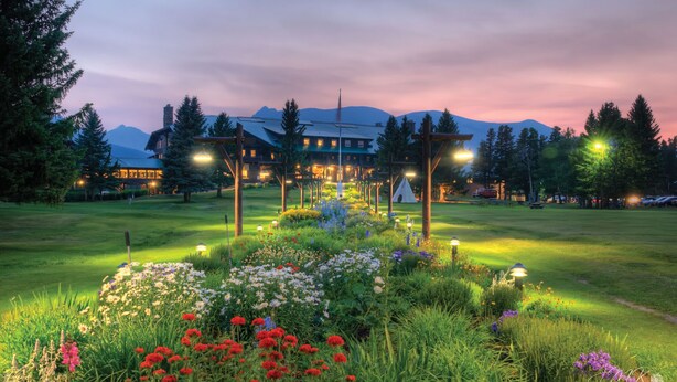 A lodge with a large building, outdoor seating, and a garden with various flowers. - Glacier Park Lodge (East Glacier Park)