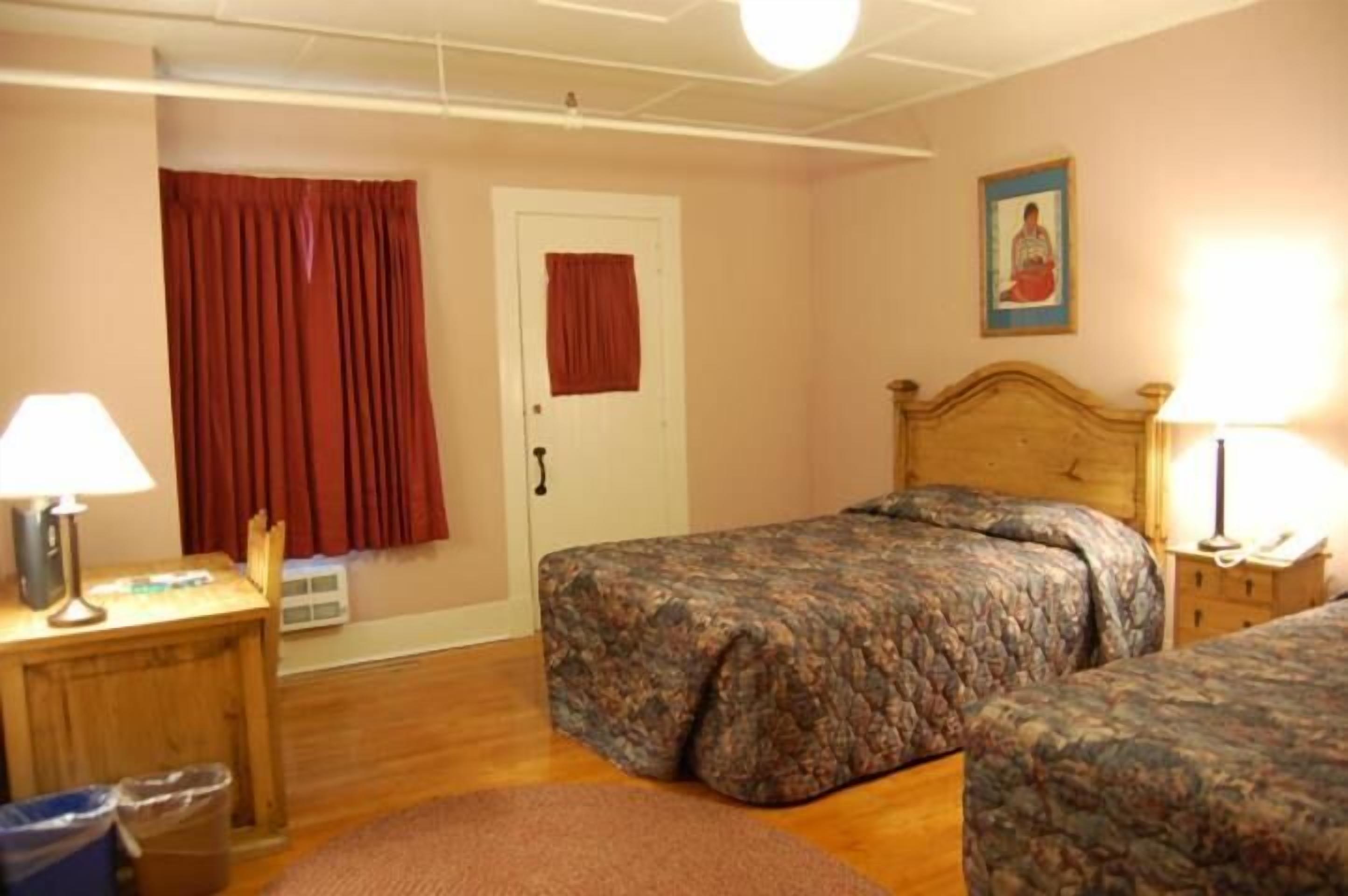 Een slaapkamer met twee bedden, een houten bureau, een stoel, een lamp en een deur met een rode gordijn.