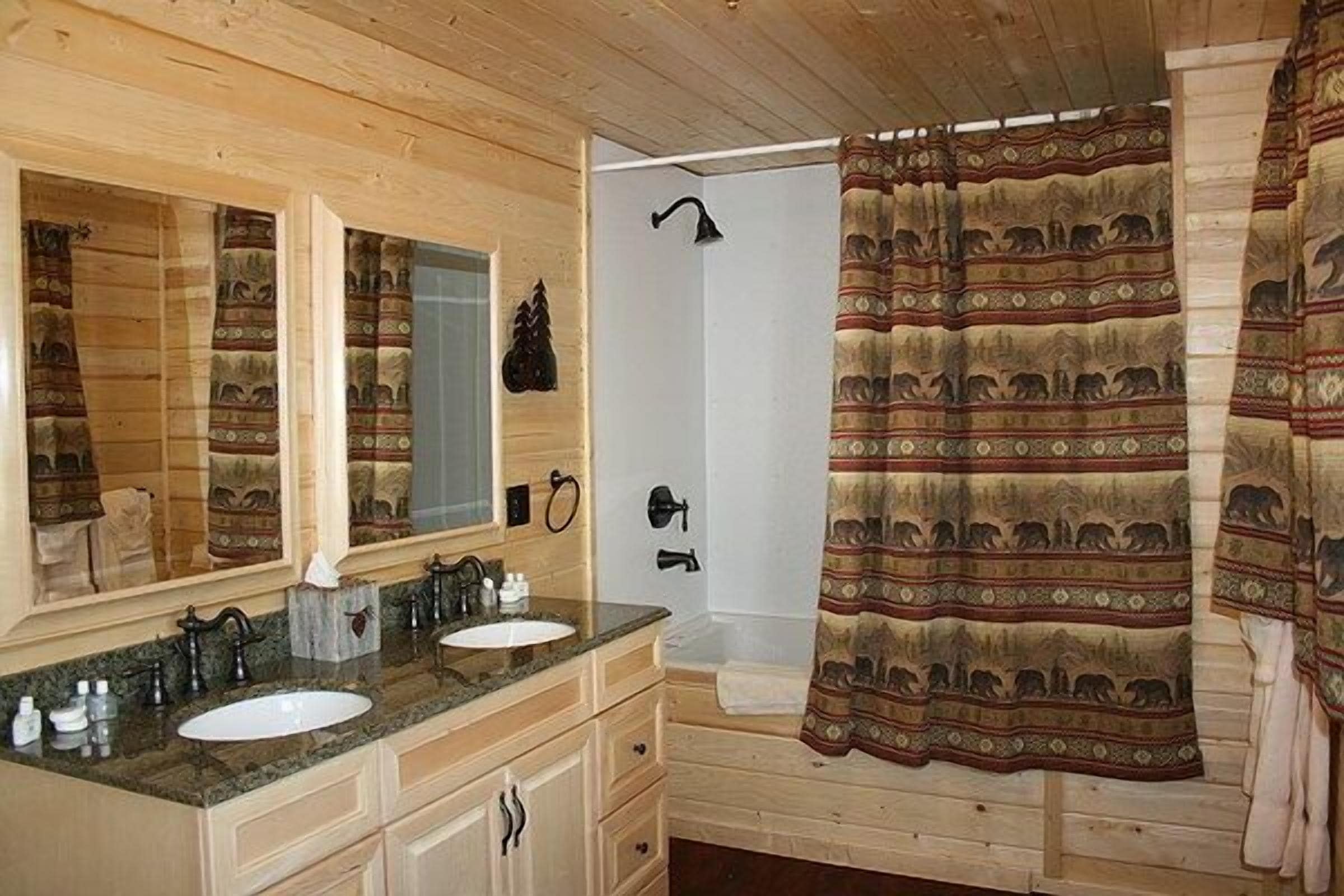 A wooden cabin bathroom with two sinks, a large mirror, a shower, and a patterned shower curtain.
