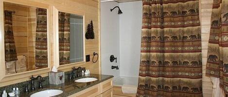 A wooden cabin bathroom with two sinks, a large mirror, a shower, and a patterned shower curtain.