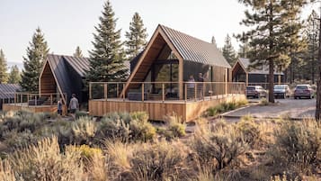 Une cabane moderne dotée d’une terrasse en bois, entourée de grands pins.