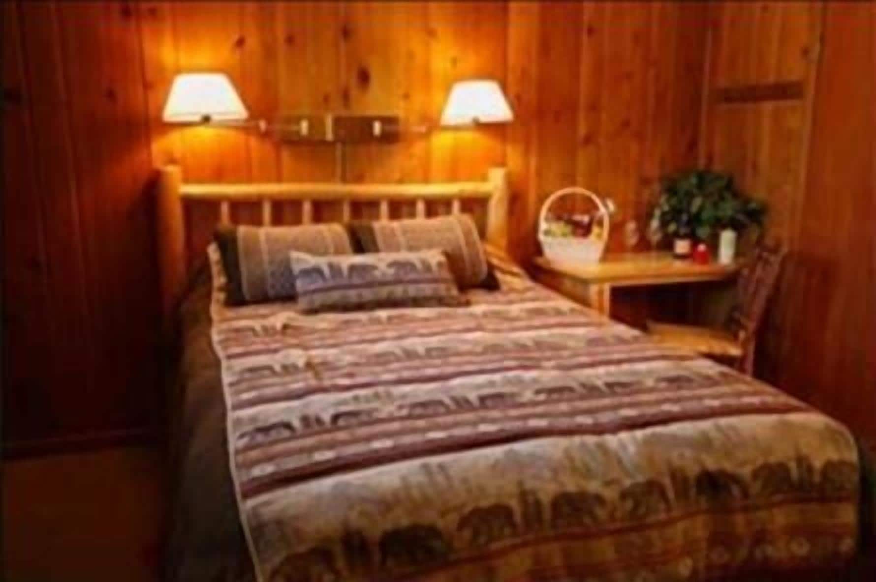 Une chambre chaleureuse avec une tête de lit en bois, un lit recouvert d’une literie à motifs, deux lampes de chevet et une petite table sur laquelle est posée une plante.