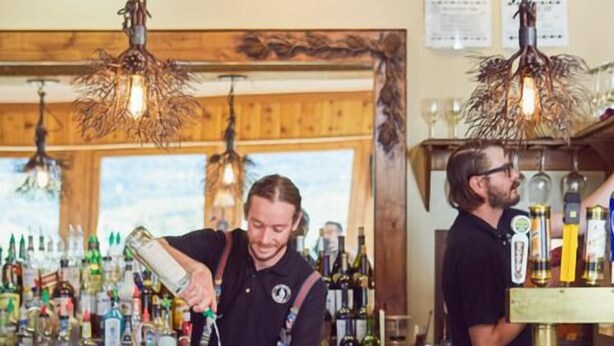 Uma área de bar com cadeiras de madeira e um bartender preparando bebidas.