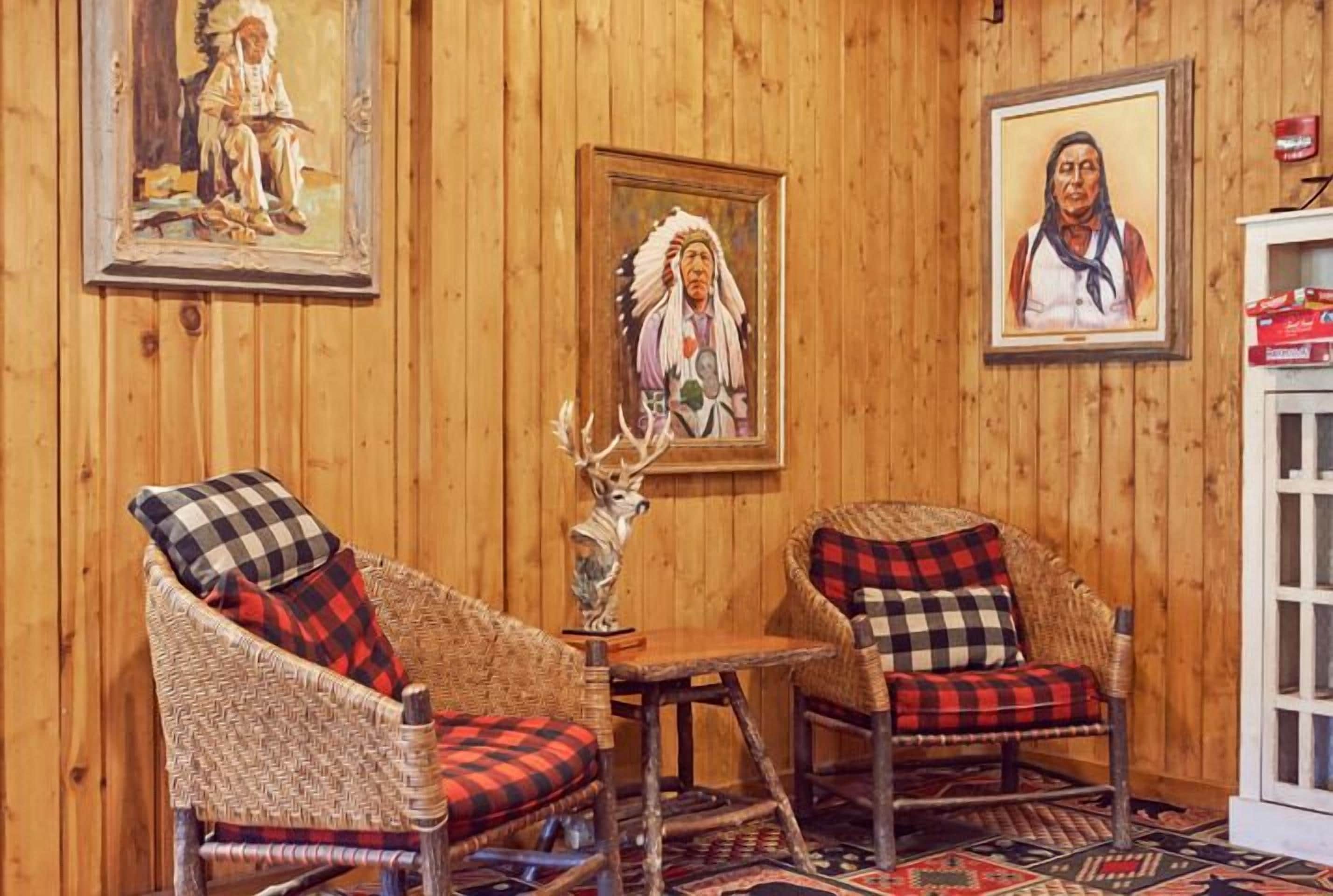 A room with wooden walls, two wicker chairs with checkered cushions, a small table, and two framed paintings.