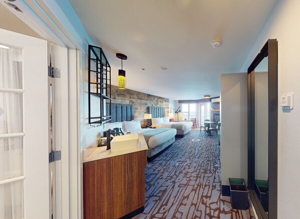 A hotel room with a bed, a desk, a chair, a small table, and a bathroom area.