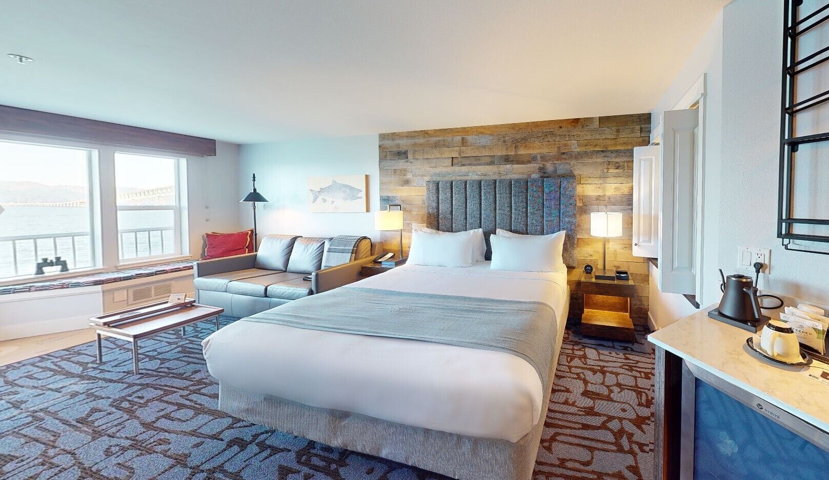 A hotel room with a large bed, a sofa, a desk, and a view of the city.