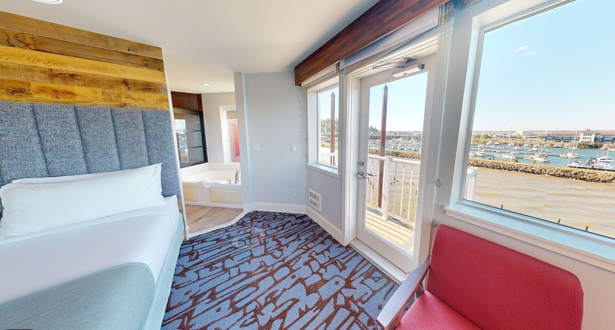 A hotel room with a bed, a bathroom, a balcony with a view of the marina.