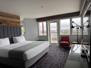 A modern hotel room with a large bed, a red armchair, a desk with a laptop, and large windows offering a city view. - Cannery Pier Hotel & Spa (Astoria)