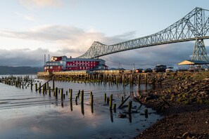 A waterfront property with a large red building, a dock extending into the water, and a bridge in the background. - Cannery Pier Hotel & Spa (Astoria)
