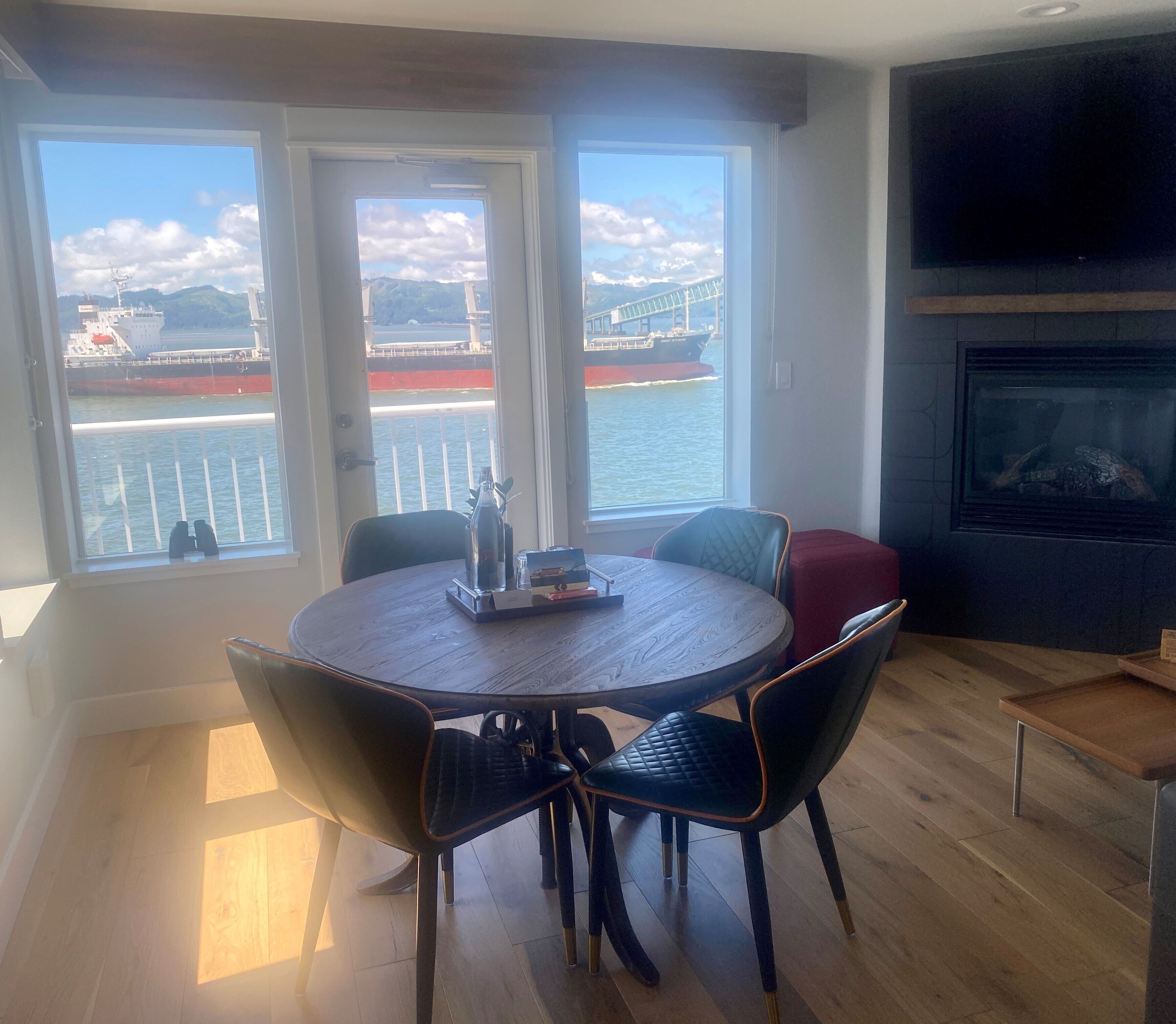 Ein Essbereich mit einem runden Tisch und Stühlen, einem Kamin und Blick auf ein Schiff auf dem Wasser durch große Fenster.