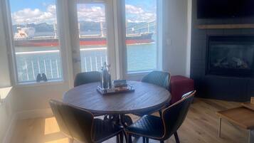 Ein Essbereich mit einem runden Tisch und Stühlen, einem Kamin und Blick auf ein Schiff auf dem Wasser durch große Fenster.