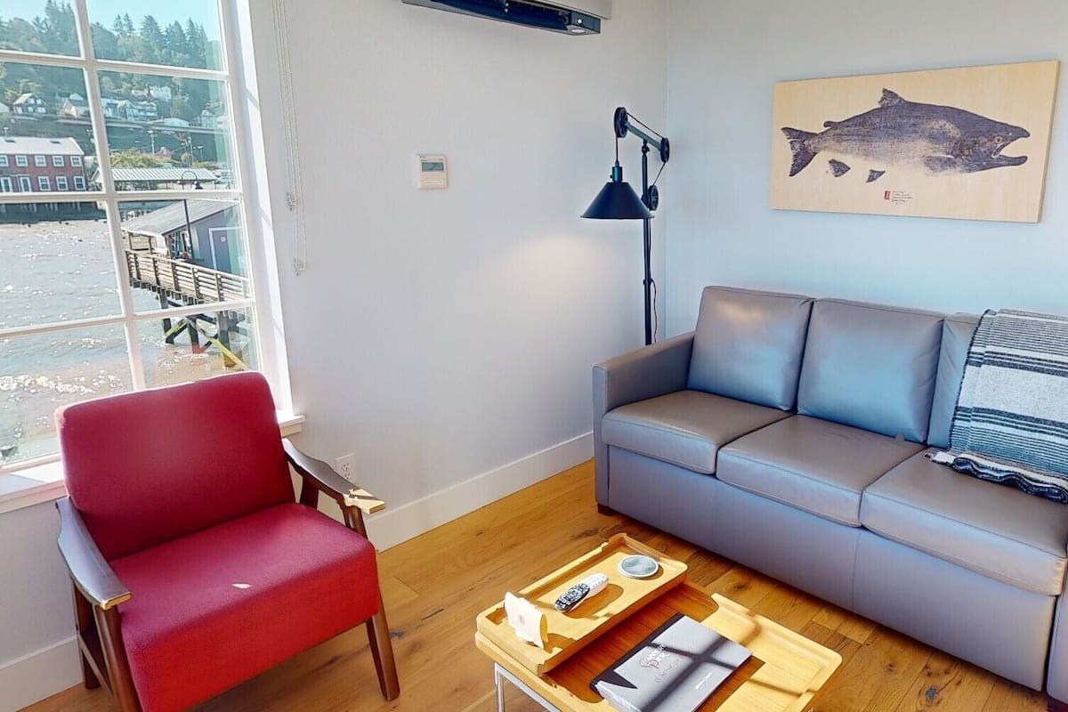A living room with a red chair, grey sofa, and a wooden coffee table with books and a remote control.