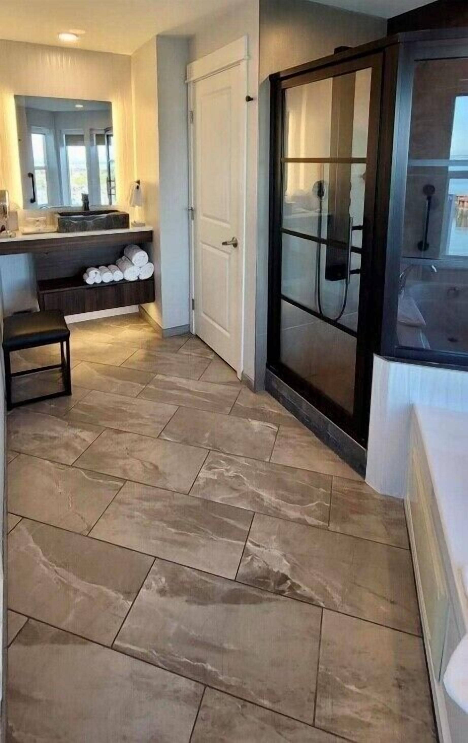 A modern bathroom with a glass shower enclosure, a white sink, and a towel rack.