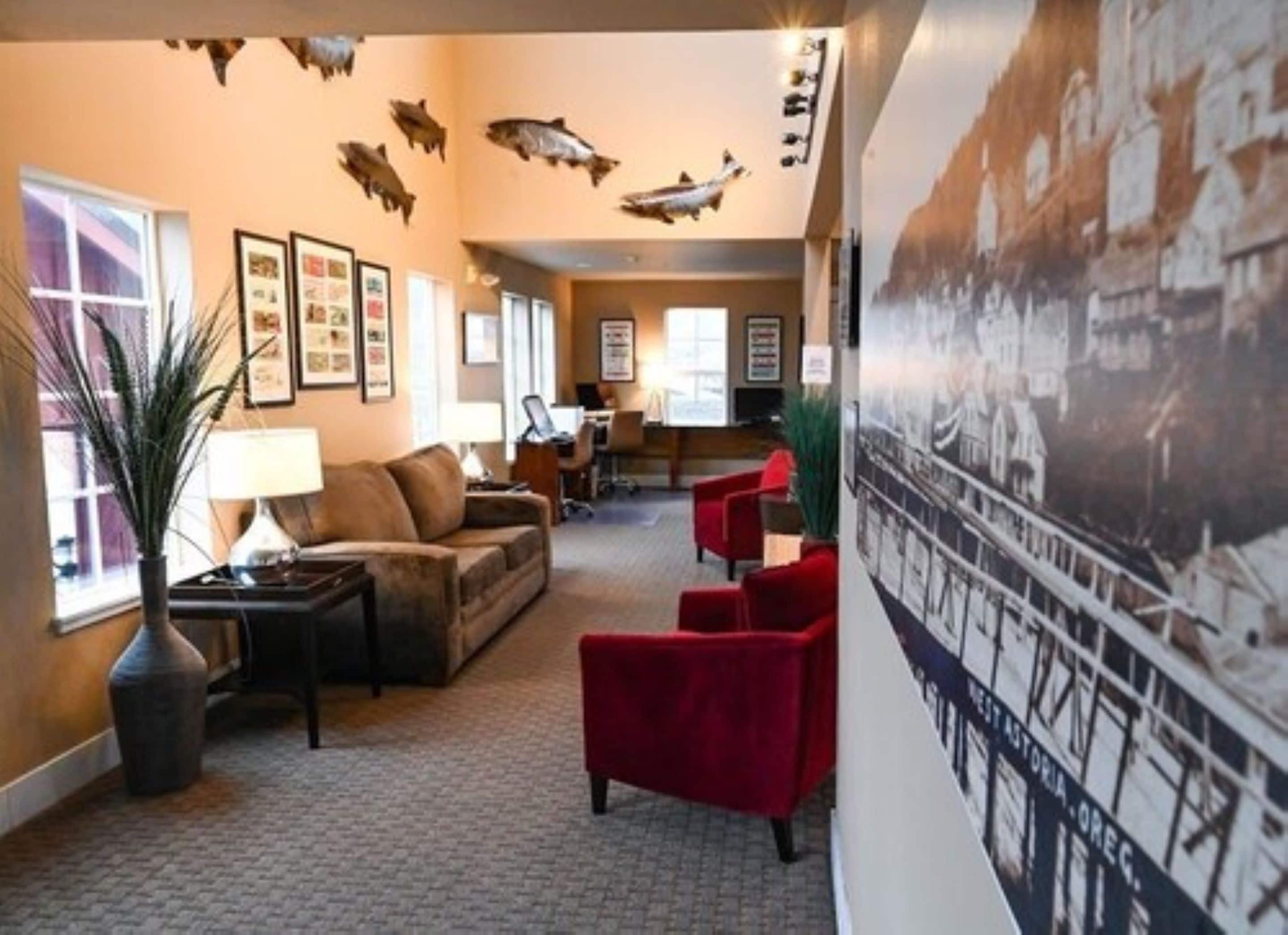 A lobby with a sofa, red chairs, a lamp, a plant, and wall art including fish and a historical building.