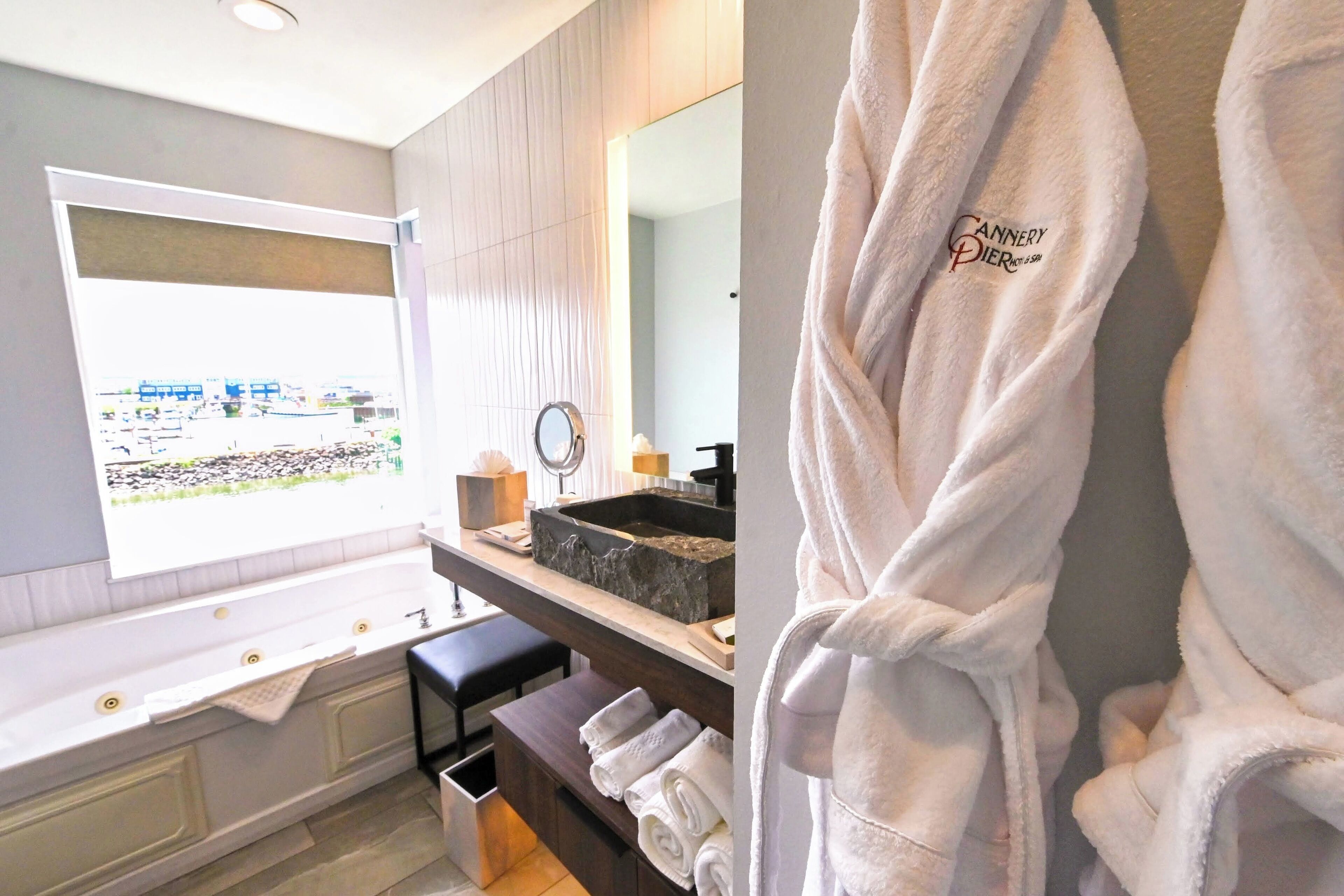 Un baño moderno con una bañera grande, un tocador con lavamanos de piedra y vistas a un paisaje urbano a través de una ventana.