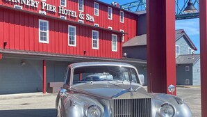 A classic car parked in front of Cannery Pier Hotel & Spa, with a red building and a large bell tower in the background.