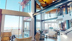 Un intérieur spacieux avec de grandes fenêtres, un plafond haut avec des poutres apparentes et un coin salon moderne.
