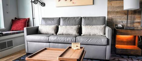 A modern living room with a grey sofa, a wooden coffee table, a red pillow, and a fish artwork on the wall.