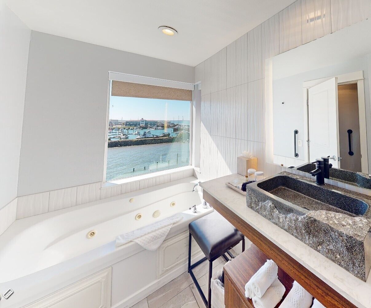 Un baño moderno con una bañera grande, un lavabo de granito y vistas a un puerto deportivo.