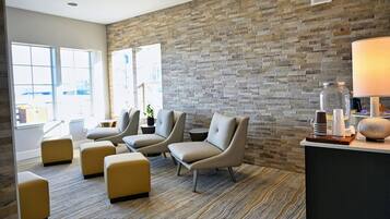 Un área de descanso moderna con sillones de cuero, alfombra estampada, pared de piedra y una recepción con lámpara y elementos decorativos.