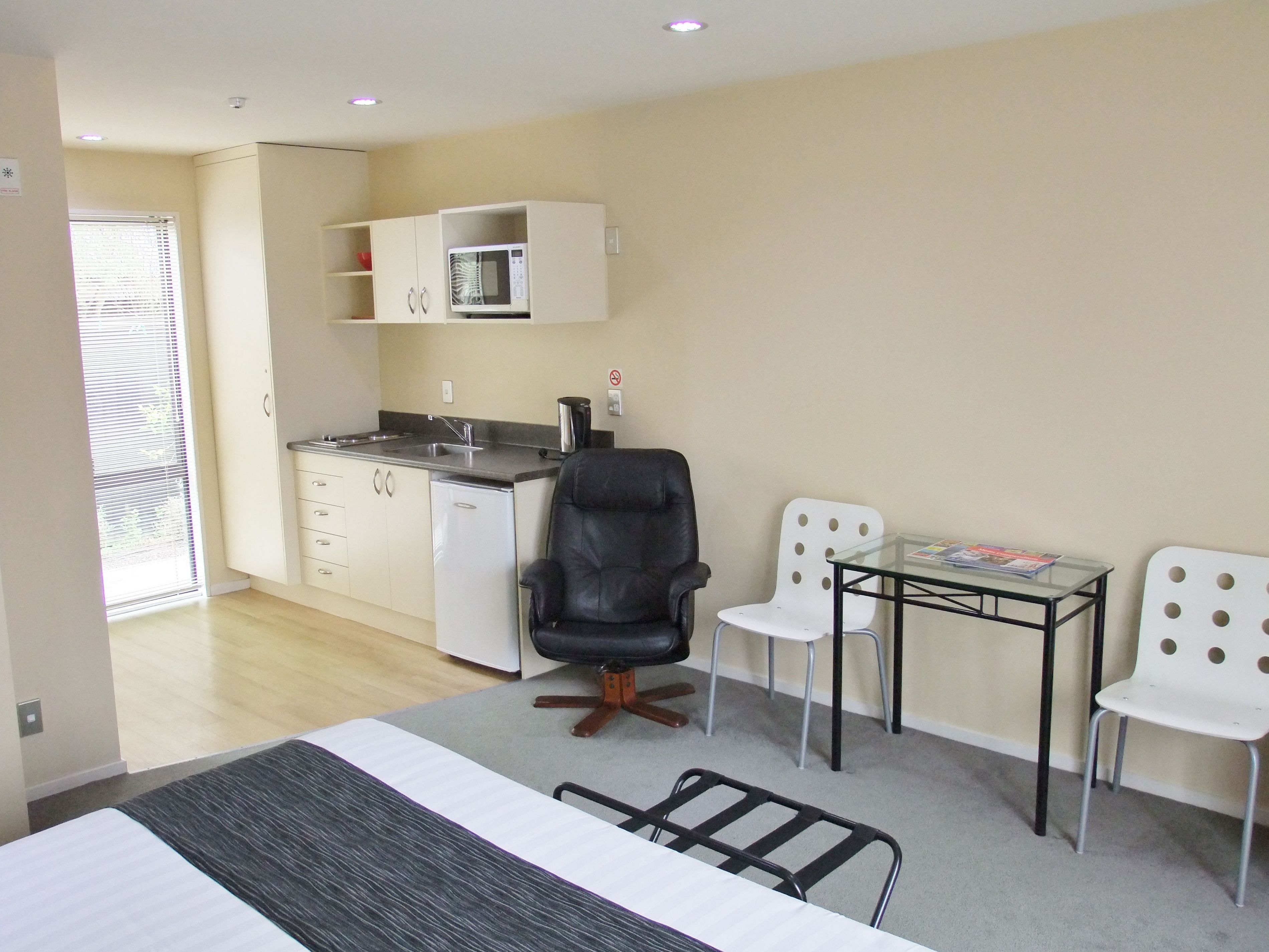 Een kleine kamer met een kitchenette, een bed en twee stoelen.