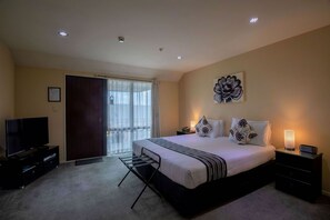 A bedroom with a large bed, a TV, a bedside table with a lamp, and a door leading to a balcony. - Abbella Lodge Motel (Christchurch)