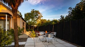 A patio with a table and chairs, surrounded by a fence and trees. - Abbella Lodge Motel (Christchurch)