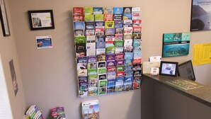 A hotel reception area with a wall display of travel brochures and a digital screen. - Abbella Lodge Motel (Christchurch)