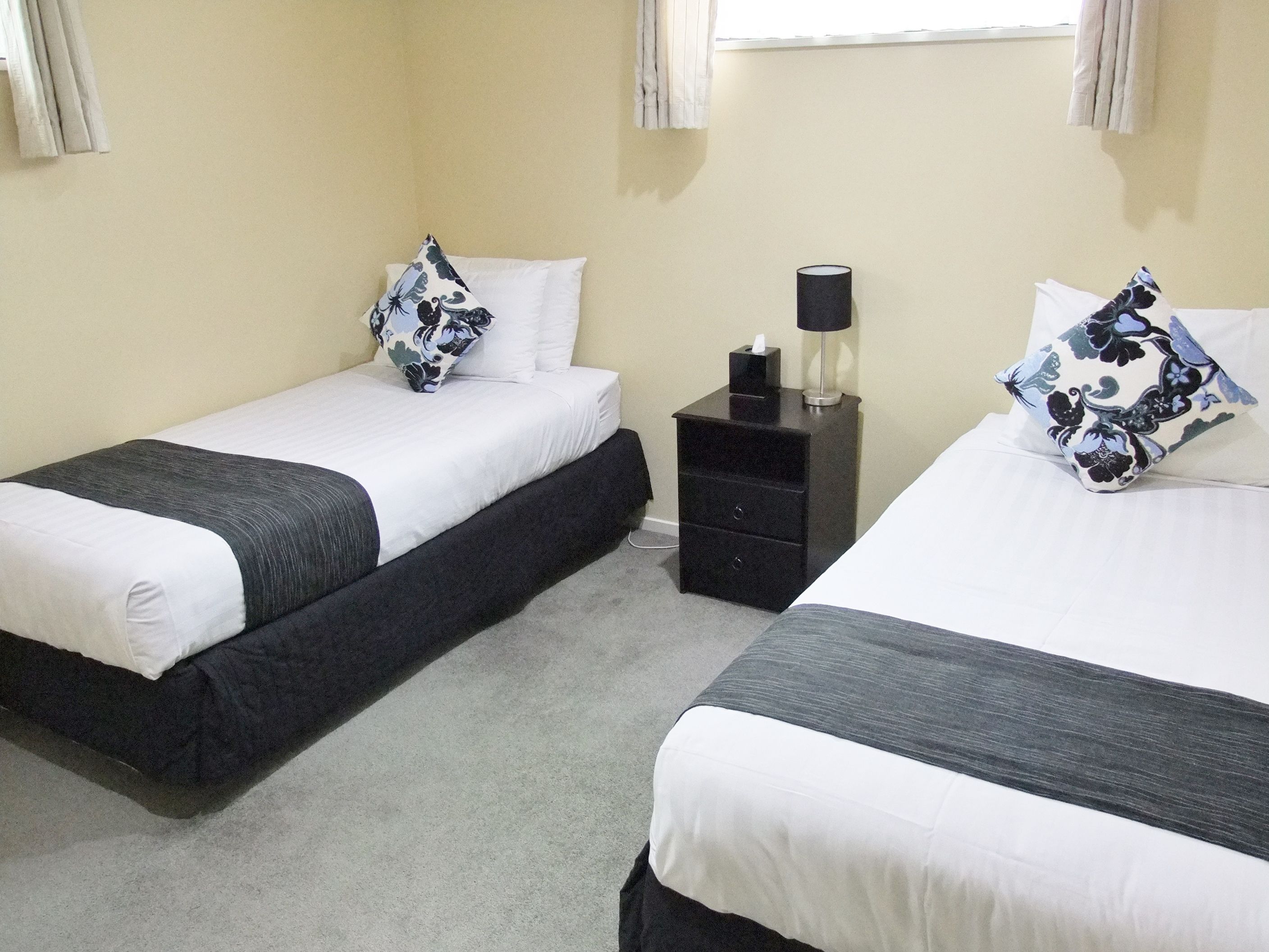 A hotel room with two single beds, a nightstand with a lamp, and a window with curtains.