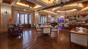 A spacious hotel lobby with wooden flooring, a central seating area with chairs, a wine cart, and a bar area with a counter and shelves.