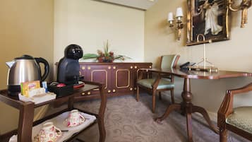A hotel room with a wooden desk, a coffee maker, a tea set, a chair, and a painting on the wall.