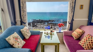 Une pièce avec deux canapés placés face à une fenêtre donnant sur la mer et une côte rocheuse.