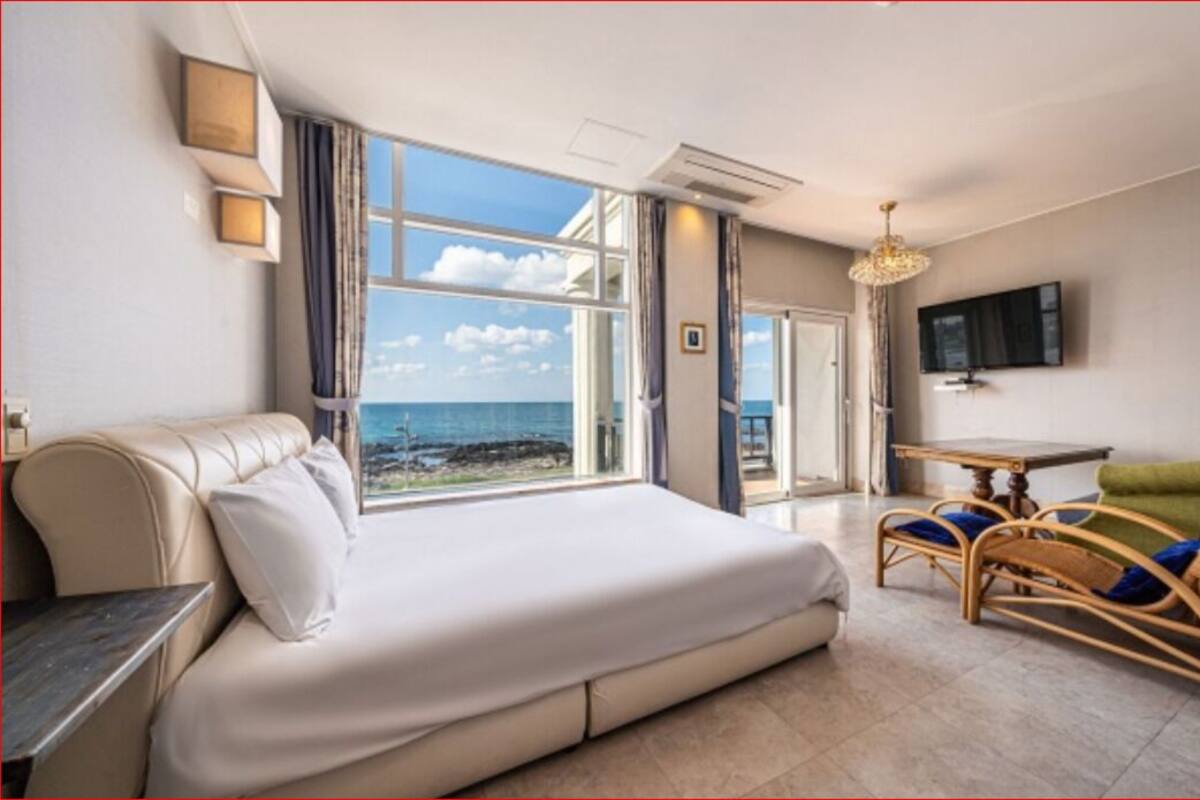 Una habitació amb llit, una cadira, una taula, televisió i vista al mar.