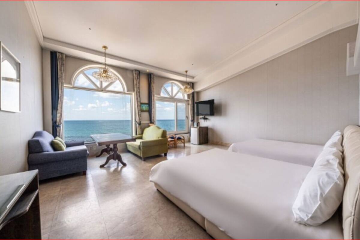 Habitació d'hotel amb un llit gran, un sofà, una cadira, un televisor i vista al mar.