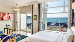 Une chambre avec un grand lit, une télévision, un bureau et une vue sur la mer.