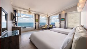 Une chambre d’hôtel dotée d’un grand lit, d’un bureau et d’une chaise, et offrant une vue sur la mer grâce à de grandes fenêtres.