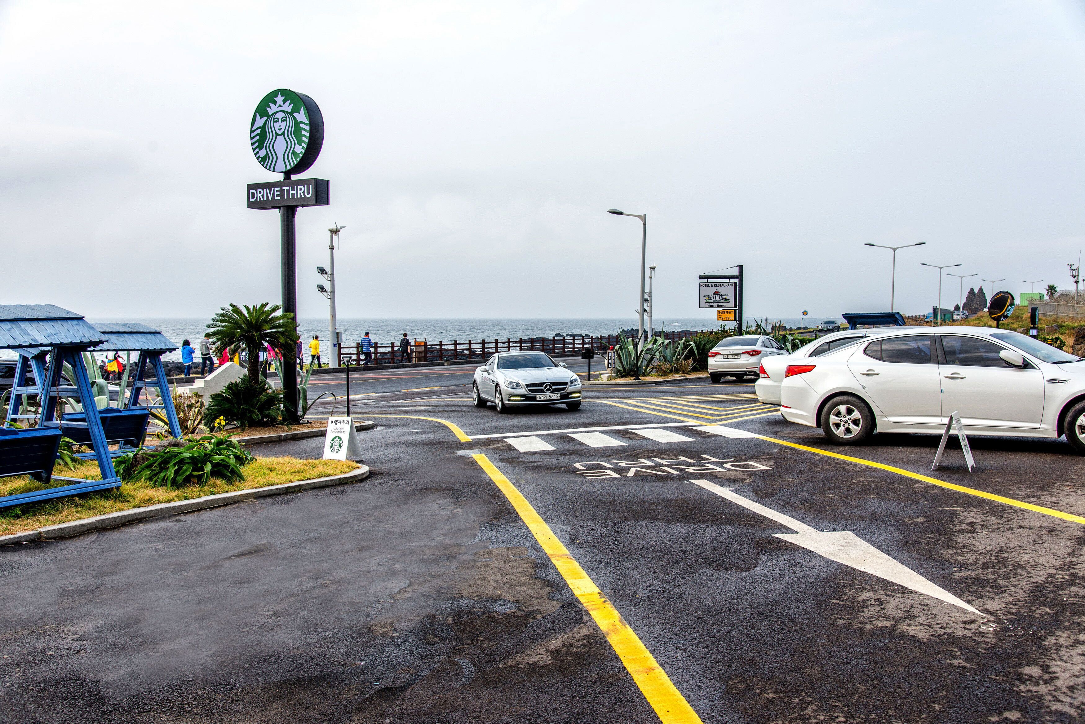 A drive-thru area with a Starbucks sign, a pedestrian crossing, and a view of the sea.