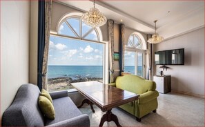 A living room with a view of the sea, a television, and a dining table. - Hotel White House (Jeju City)