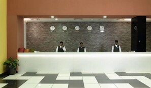 A reception desk with three staff members, a clock wall, and a checkered floor. - Wonderla Resort (Ramanagara)