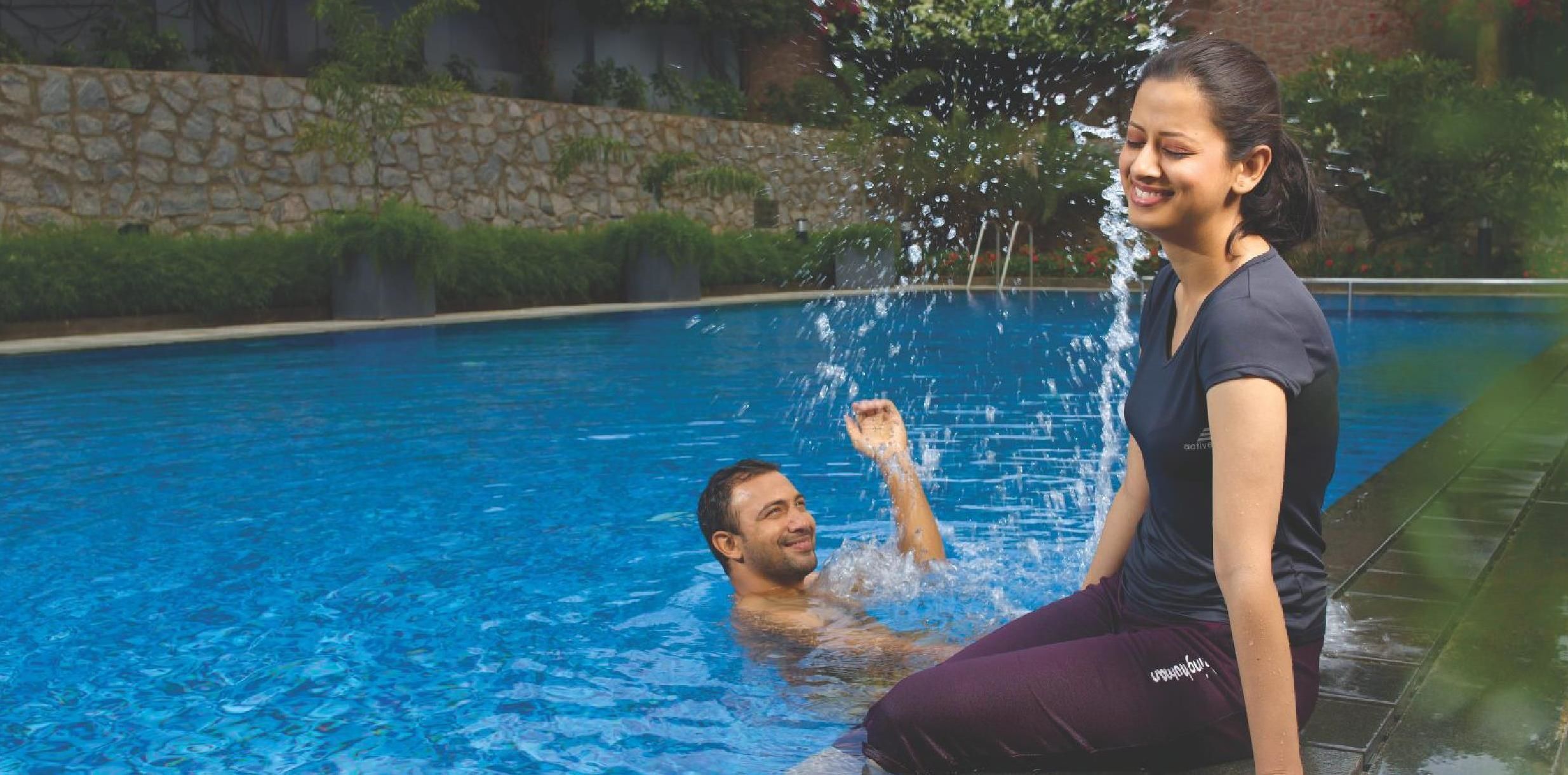 En swimmingpool med kristallklart blått vatten, omgiven av en stenmur och grönska.