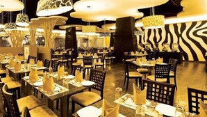 A restaurant with multiple tables and chairs, each set with a napkin and a glass. - Wonderla Resort (Ramanagara)