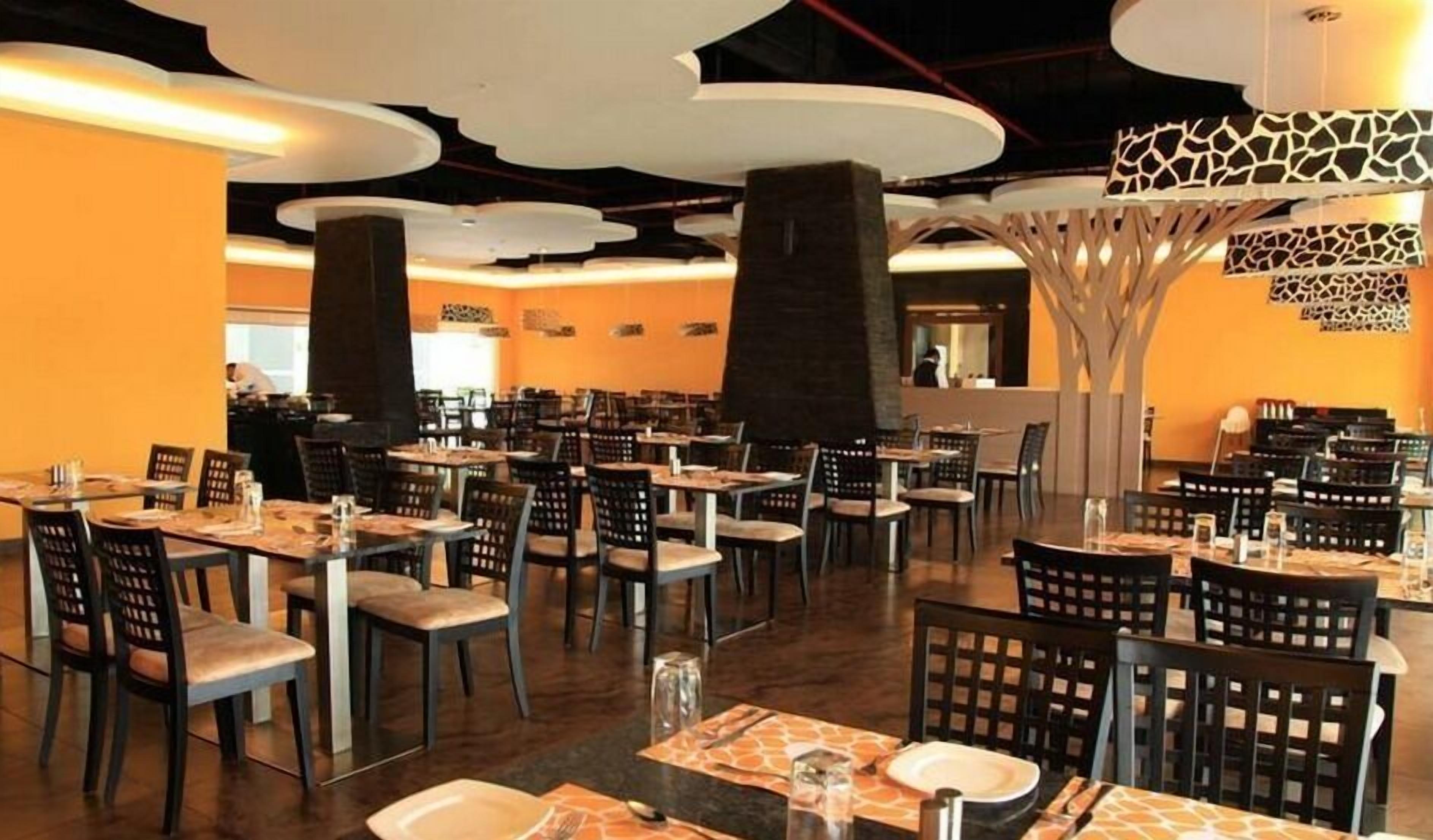 A spacious restaurant with multiple tables and chairs, a modern ceiling design, and a central decorative structure.